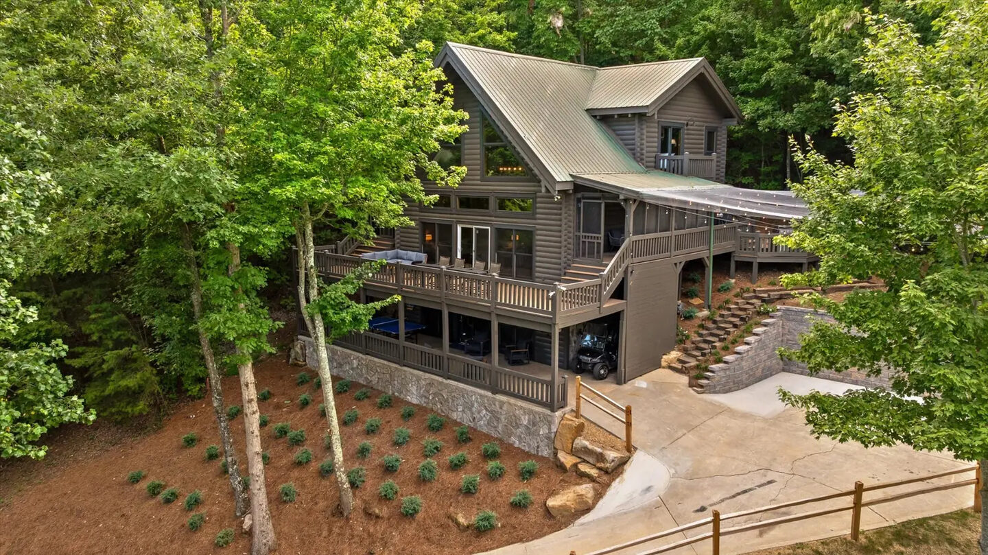 The Eyrie House, a three-story cabin under a standing-seam metal roof, with covered decks on every level, a golf cart parked underneath and a concrete drive at right