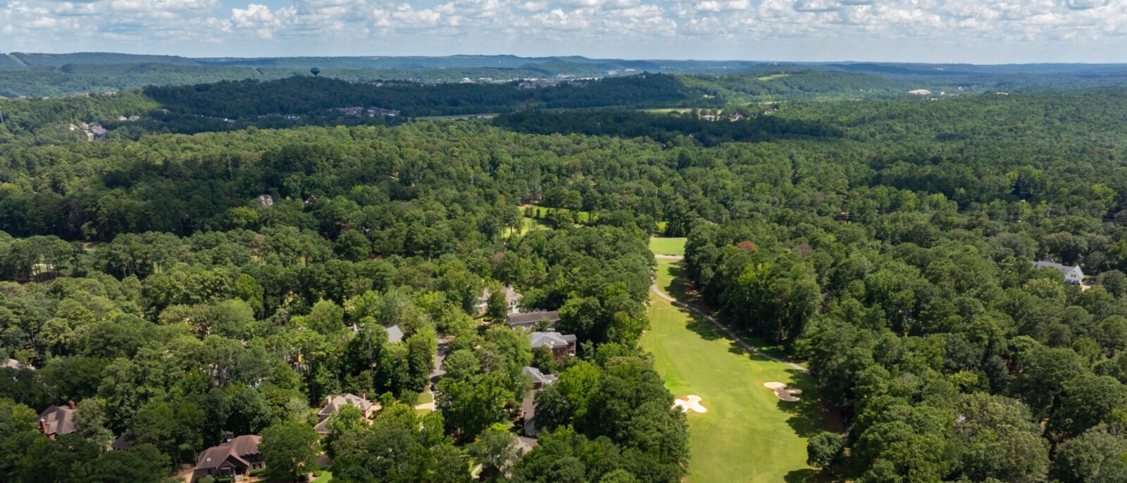 Aerial view of a Riverchase fairway running between wooded homes, with the Hoover ridge line in the distance